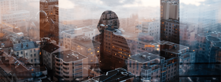 Reflection of a woman looking out a window over a large city from a tall building.