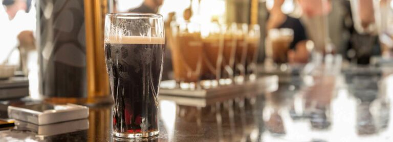 Glasses of stout beer on a bar counter, blurred people, panoramic pub header